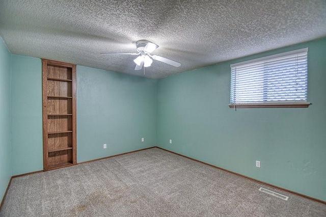 carpeted spare room with a textured ceiling, built in shelves, visible vents, baseboards, and a ceiling fan