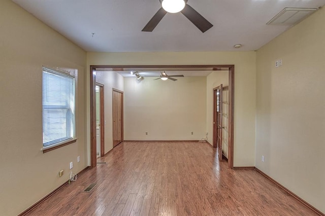 empty room featuring a ceiling fan, visible vents, baseboards, and wood finished floors