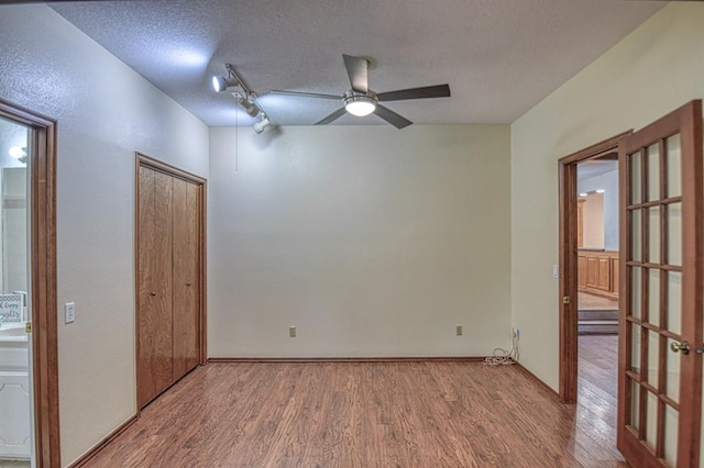 unfurnished bedroom with a closet, a textured ceiling, track lighting, wood finished floors, and baseboards