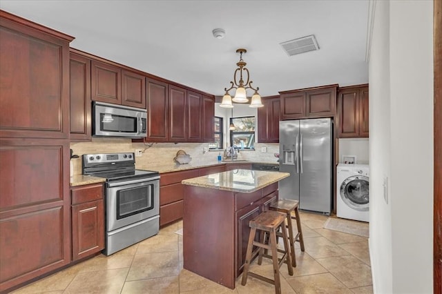 kitchen featuring appliances with stainless steel finishes, tasteful backsplash, pendant lighting, washer / dryer, and a kitchen island