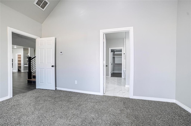 unfurnished bedroom featuring carpet, a walk in closet, and high vaulted ceiling