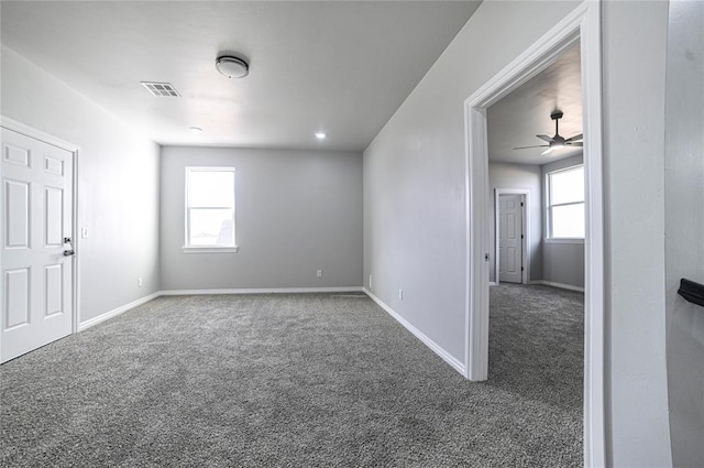 spare room with a wealth of natural light, ceiling fan, and dark colored carpet