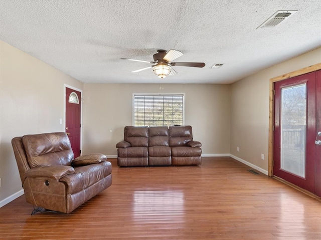 living room featuring ceiling fan, a textured ceiling, and light wood-type flooring