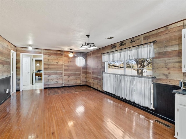 unfurnished living room featuring wooden walls, ceiling fan, and hardwood / wood-style flooring