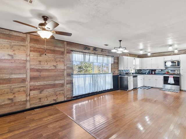 kitchen with decorative backsplash, appliances with stainless steel finishes, ceiling fan, white cabinets, and hardwood / wood-style floors