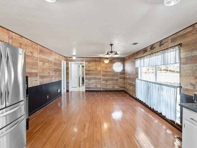 interior space with wooden walls, a ceiling fan, freestanding refrigerator, dark countertops, and light wood-type flooring