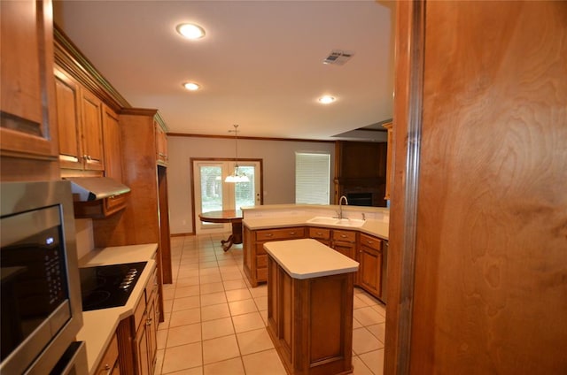 kitchen with pendant lighting, stainless steel microwave, sink, black stovetop, and a kitchen island