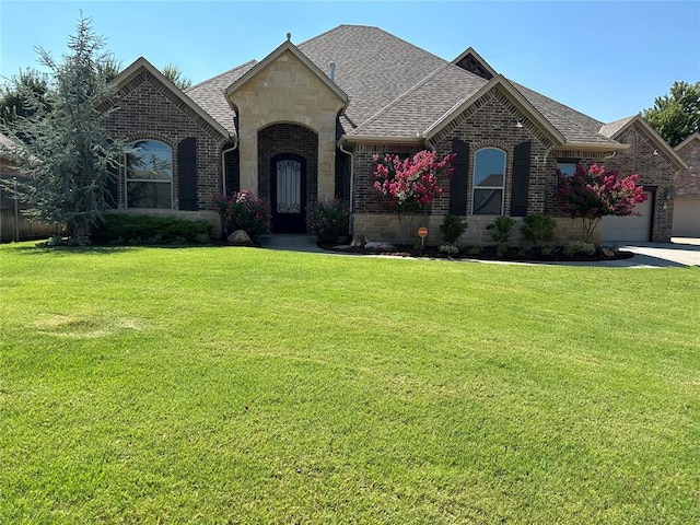 french country inspired facade with a front yard, brick siding, and a shingled roof