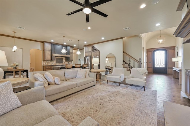 living room with arched walkways, visible vents, and ornamental molding