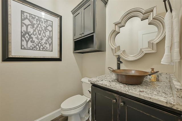 half bathroom featuring vanity, toilet, and baseboards