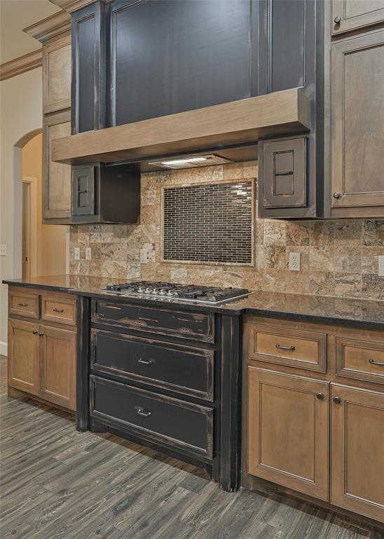 kitchen featuring dark wood finished floors, arched walkways, stainless steel gas stovetop, wall chimney range hood, and backsplash