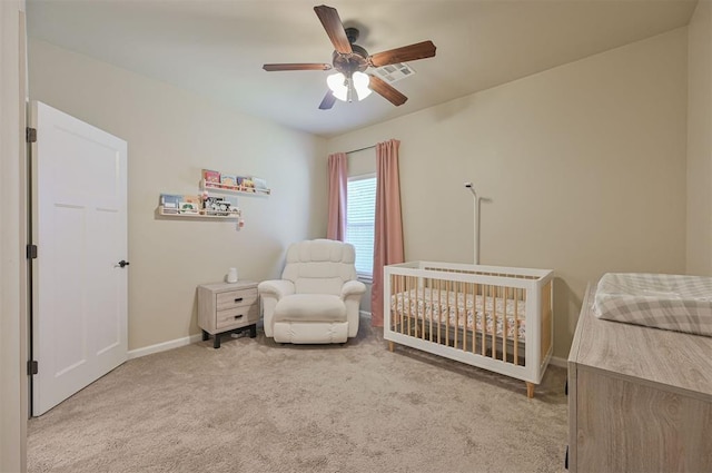 carpeted bedroom with a crib, baseboards, and a ceiling fan