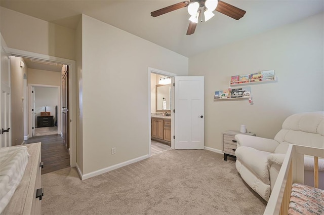 bedroom featuring a ceiling fan, baseboards, a sink, ensuite bathroom, and light carpet