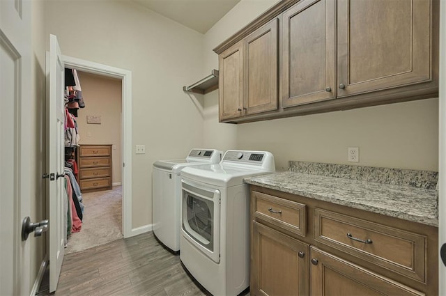 washroom featuring wood finished floors, baseboards, cabinet space, and washing machine and dryer