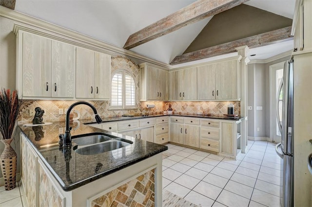 kitchen featuring stainless steel refrigerator, sink, tasteful backsplash, lofted ceiling with beams, and dark stone counters