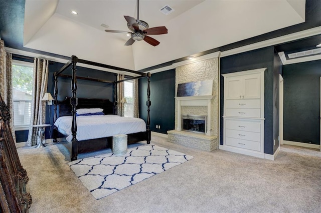 bedroom featuring a raised ceiling, ceiling fan, a large fireplace, and light carpet