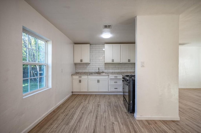 kitchen featuring backsplash, sink, light hardwood / wood-style flooring, black gas stove, and white cabinetry