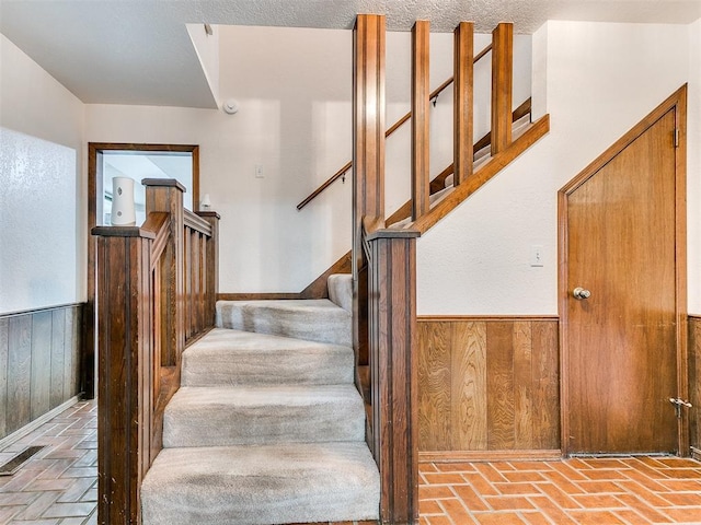 stairs with a textured ceiling and wood walls