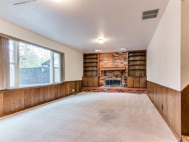 unfurnished living room with a textured ceiling, carpet floors, and wood walls