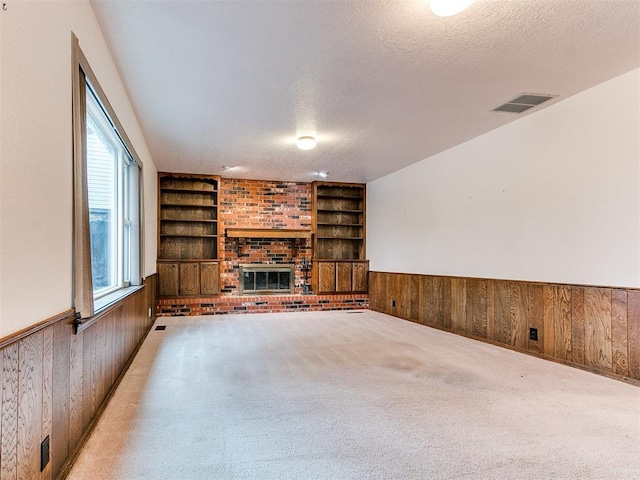 unfurnished living room featuring wood walls, a fireplace, light colored carpet, and a textured ceiling