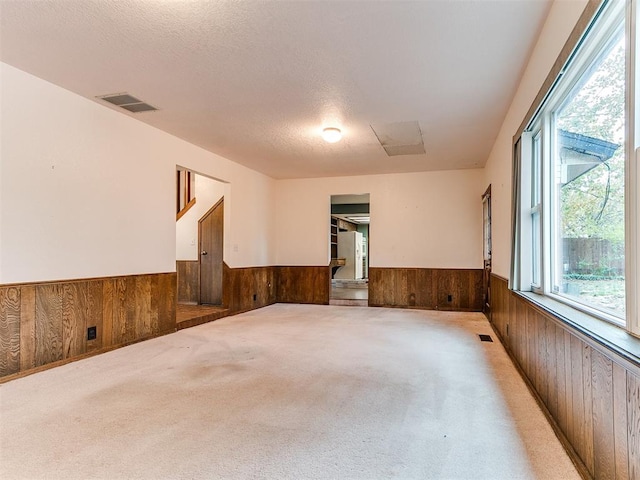 unfurnished room with a textured ceiling, light colored carpet, and wooden walls