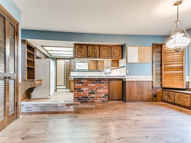 kitchen with white appliances, sink, light hardwood / wood-style flooring, hanging light fixtures, and wood walls