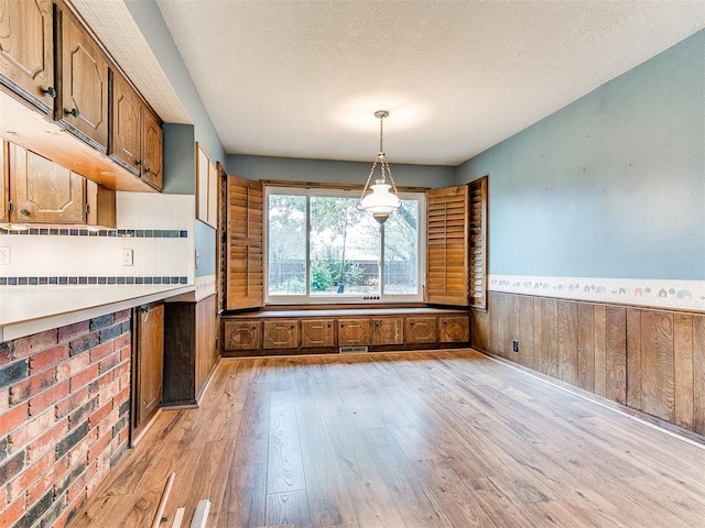 kitchen with pendant lighting, wood walls, a textured ceiling, and light hardwood / wood-style flooring