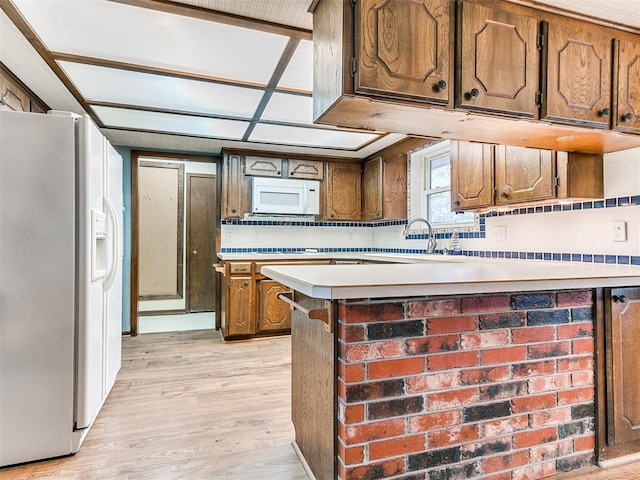 kitchen featuring sink, tasteful backsplash, light hardwood / wood-style flooring, kitchen peninsula, and white appliances