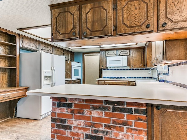 kitchen with kitchen peninsula, white appliances, light hardwood / wood-style flooring, and sink