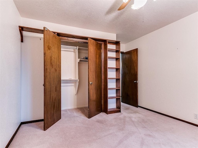 unfurnished bedroom featuring a closet, a textured ceiling, light colored carpet, and ceiling fan