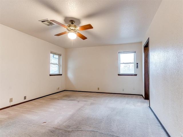 unfurnished room with ceiling fan, a healthy amount of sunlight, light colored carpet, and a textured ceiling