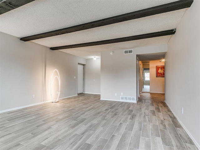 unfurnished room with beamed ceiling, a textured ceiling, and light hardwood / wood-style flooring