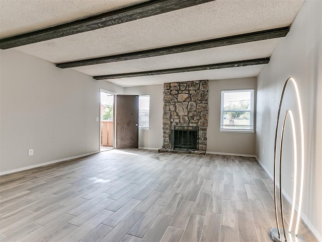 unfurnished living room featuring a stone fireplace, a healthy amount of sunlight, a textured ceiling, and light hardwood / wood-style floors