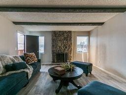 living room with beam ceiling, a fireplace, a textured ceiling, and hardwood / wood-style flooring