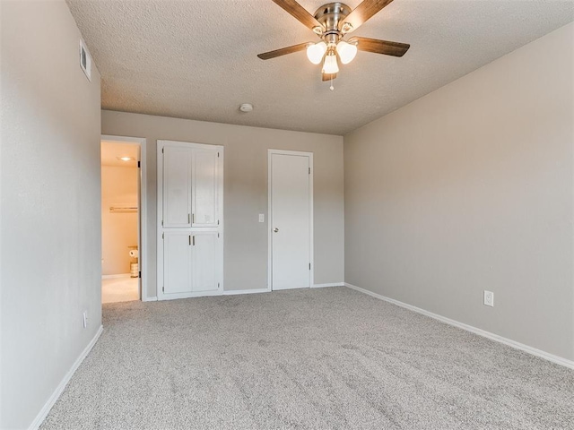 unfurnished bedroom with ceiling fan, light carpet, a textured ceiling, and ensuite bath