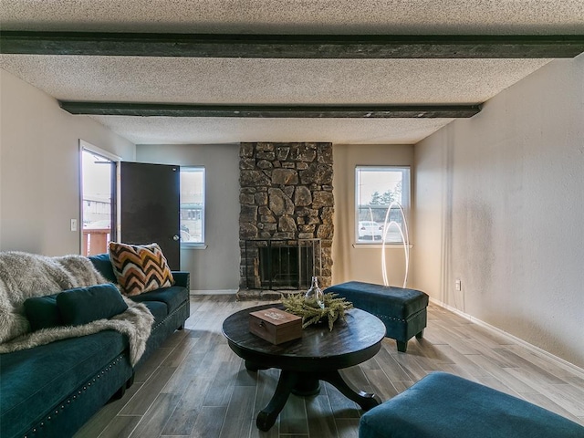 living room with beam ceiling, wood-type flooring, a stone fireplace, and a textured ceiling