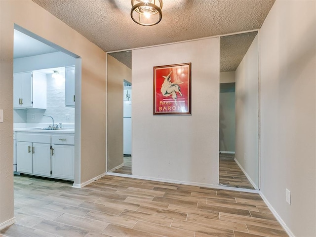 hallway featuring a textured ceiling, baseboards, a sink, and wood finish floors