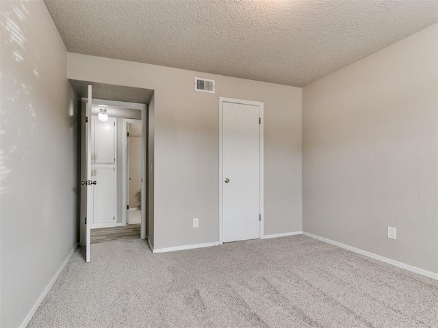 unfurnished bedroom featuring a textured ceiling, carpet floors, visible vents, and baseboards