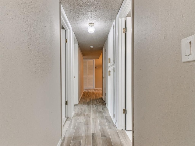 hallway featuring a textured ceiling, a textured wall, and wood tiled floor