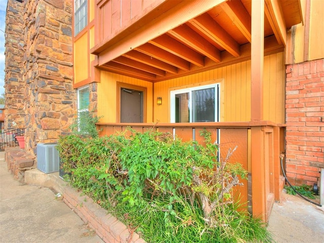 property entrance with stone siding, central AC unit, and brick siding