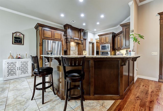 kitchen with a kitchen bar, light stone countertops, appliances with stainless steel finishes, and crown molding