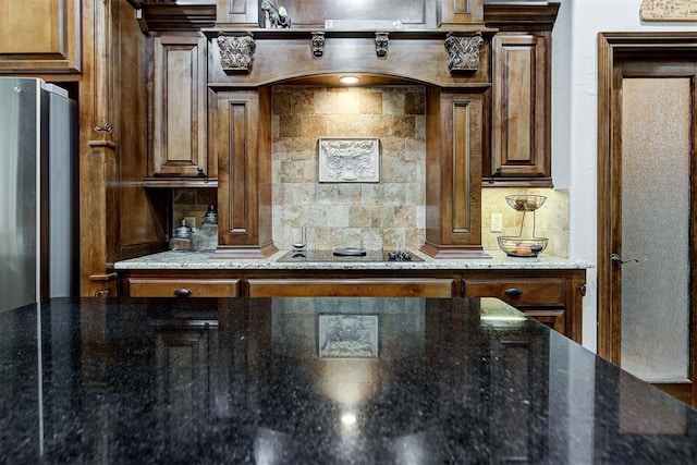 kitchen with tasteful backsplash, dark stone countertops, freestanding refrigerator, and black electric cooktop