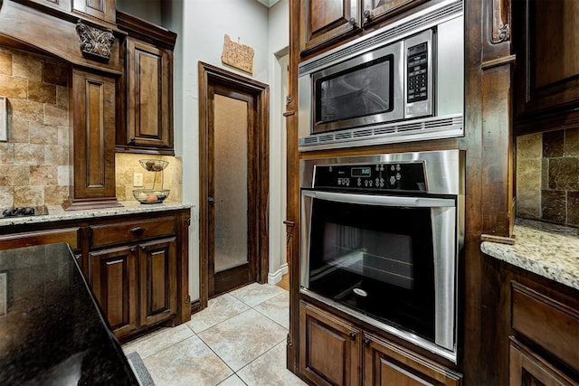 kitchen with light stone counters, backsplash, appliances with stainless steel finishes, light tile patterned floors, and dark brown cabinets