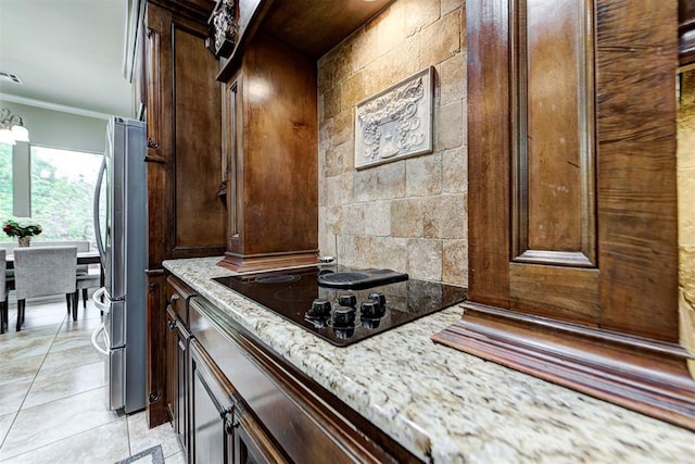 kitchen featuring light stone counters, freestanding refrigerator, ornamental molding, dark brown cabinetry, and black electric stovetop