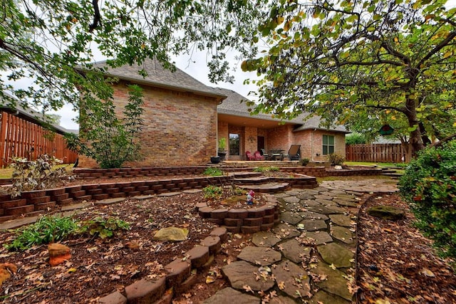 back of house featuring a patio, brick siding, fence private yard, and a shingled roof