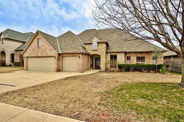 french country style house with an attached garage, concrete driveway, roof with shingles, and fence