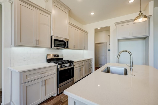 kitchen with pendant lighting, appliances with stainless steel finishes, tasteful backsplash, sink, and a kitchen island with sink