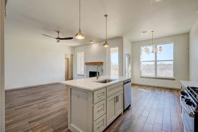 kitchen featuring ceiling fan with notable chandelier, pendant lighting, appliances with stainless steel finishes, sink, and a center island with sink