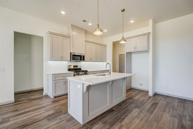 kitchen with hanging light fixtures, appliances with stainless steel finishes, sink, backsplash, and a kitchen island with sink