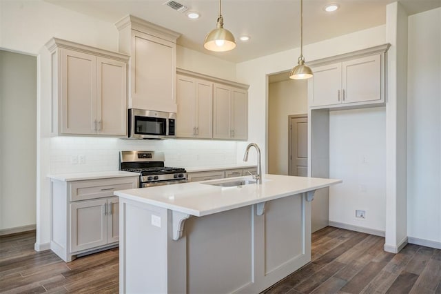 kitchen with appliances with stainless steel finishes, sink, decorative light fixtures, a center island with sink, and dark hardwood / wood-style floors